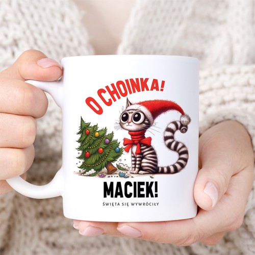 Biały kubek z kotem w czapce Mikołaja i choinką to zabawny personalizowany prezent świąteczny.