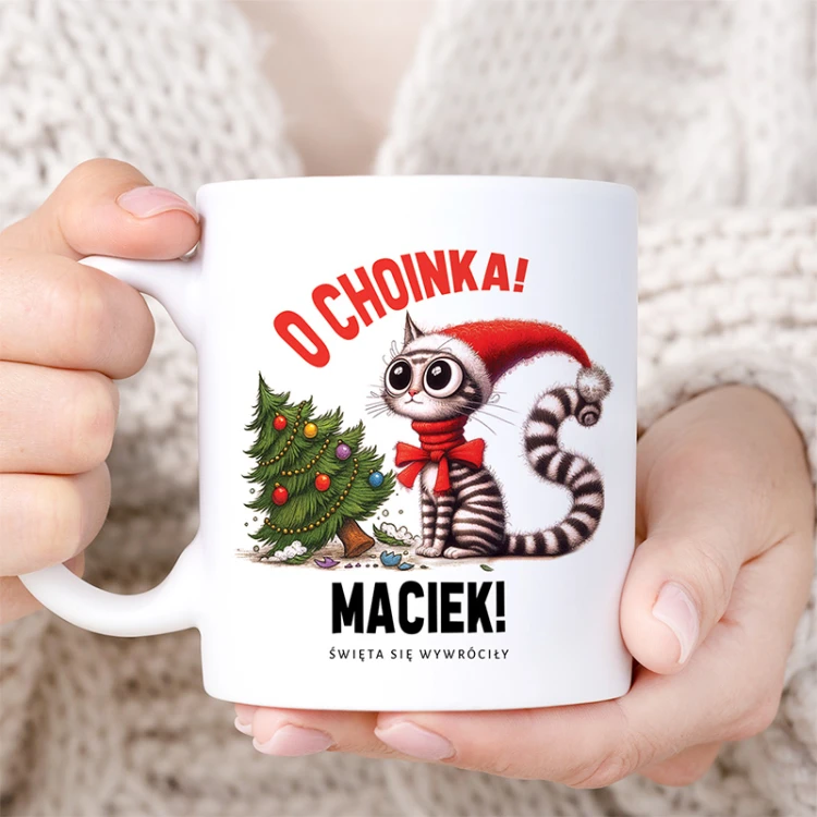 Biały kubek z kotem w czapce Mikołaja i choinką to zabawny personalizowany prezent świąteczny.
